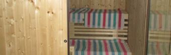 Zu sehen ist der Blick durch die Tür einer Sauna auf zwei Bänke. Auf den Bänken liegen gestreifte Handtücher.