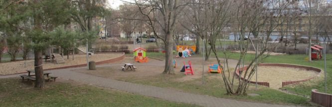 Zu sehen ist der Blick in einen weiten Garten mit viel Baumbestand. Man sieht zwei große, rund angelegte Sandkästen udn mehrere Spielgeräte für Kleinstkinder.